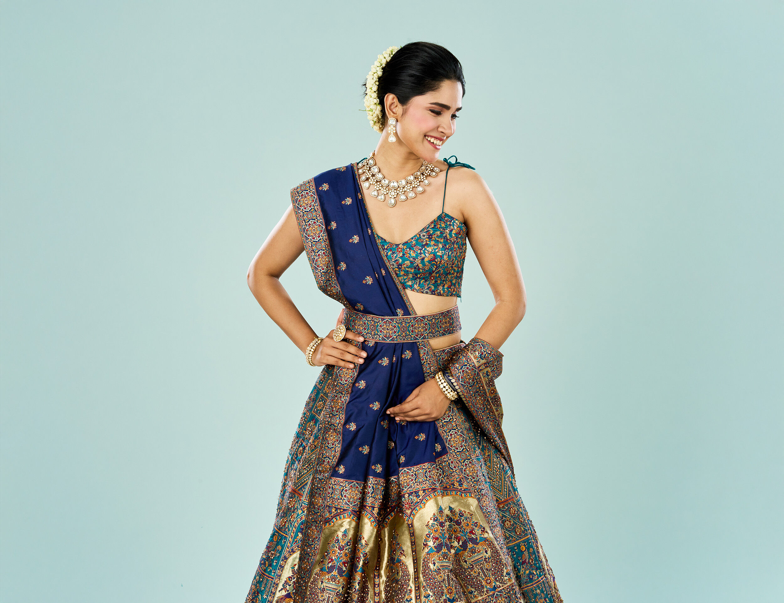 Bride in multicolour threadwork lehenga with royal blue dupatta and golden embroidery, styled with statement choker and jasmine flower bun
